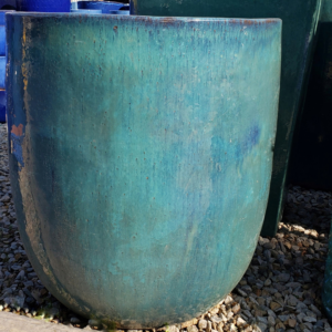 Large turquoise ceramic pot with a rustic glaze finish, displayed on gravel ground.