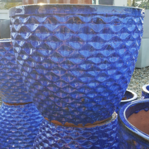 Vibrant blue ceramic pot with a textured wave pattern, set outdoors on gravel.
