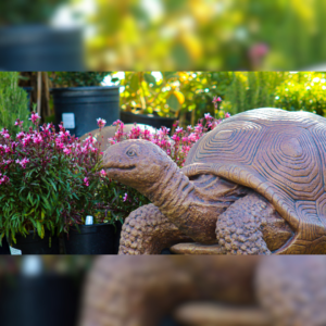 A decorative stone tortoise sculpture displayed among blooming pink flowers in a garden setting.