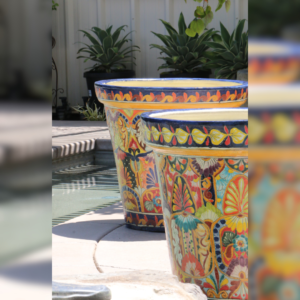 Two vibrant, hand-painted Talavera pots with intricate floral designs sitting poolside, surrounded by lush greenery.