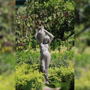 Elegant stone statue of a woman holding a water jug above her head, surrounded by lush green plants and trees.