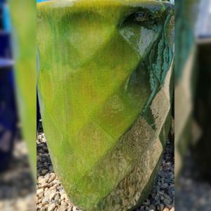 A vibrant green ceramic garden pot with a glossy finish, featuring a textured diamond pattern, placed on gravel.